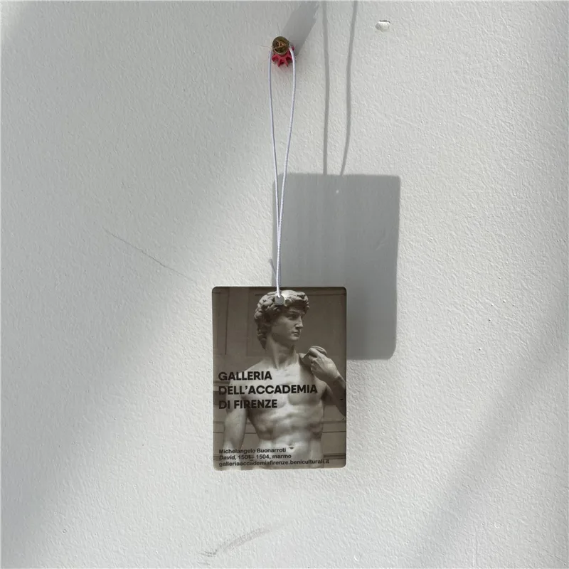Clear acrylic keychain printed with a museum-tag design, hanging against a white wall