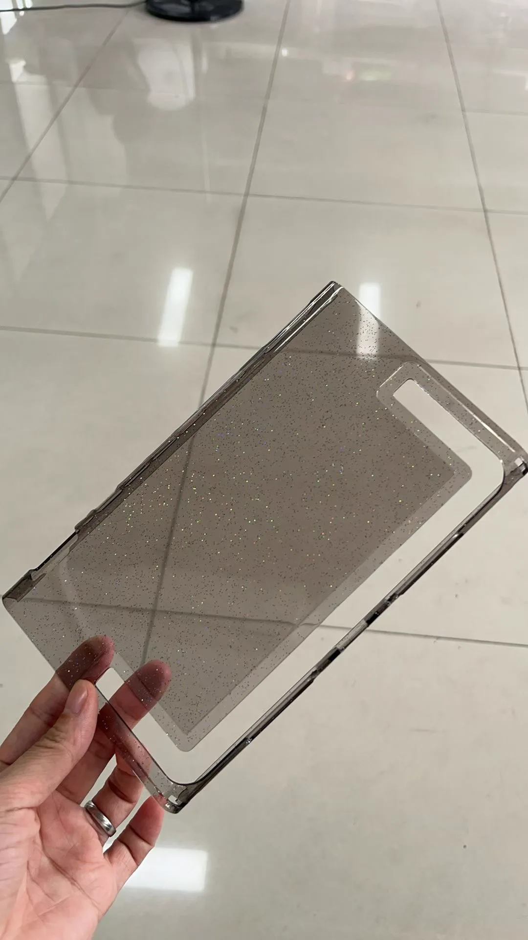 Smoke-tinted transparent Nintendo Switch 2 back-shell sample held in one hand